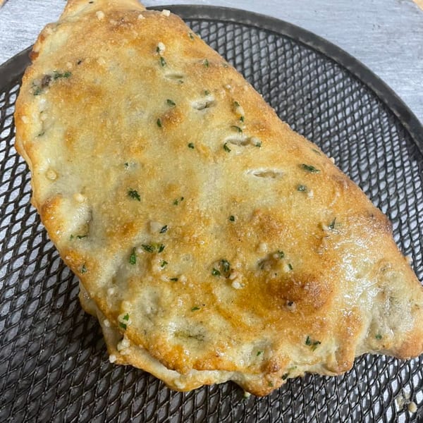 Golden-brown calzone with herbs and garlic, resting on a dark metal pizza screen.