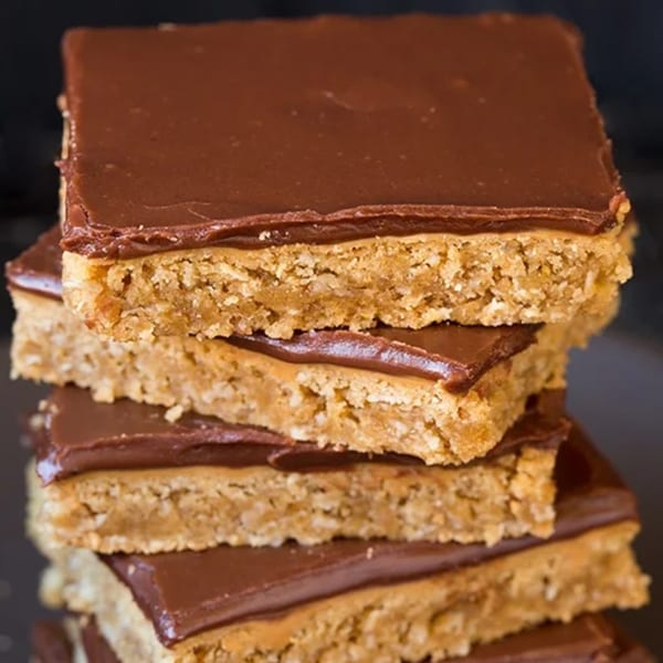 A stack of four square dessert bars with a thick chocolate topping and a light brown base.