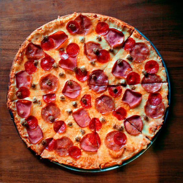 Only Pans' pepperoni, ham, and sausage pizza, sliced and ready to eat on a wooden table.