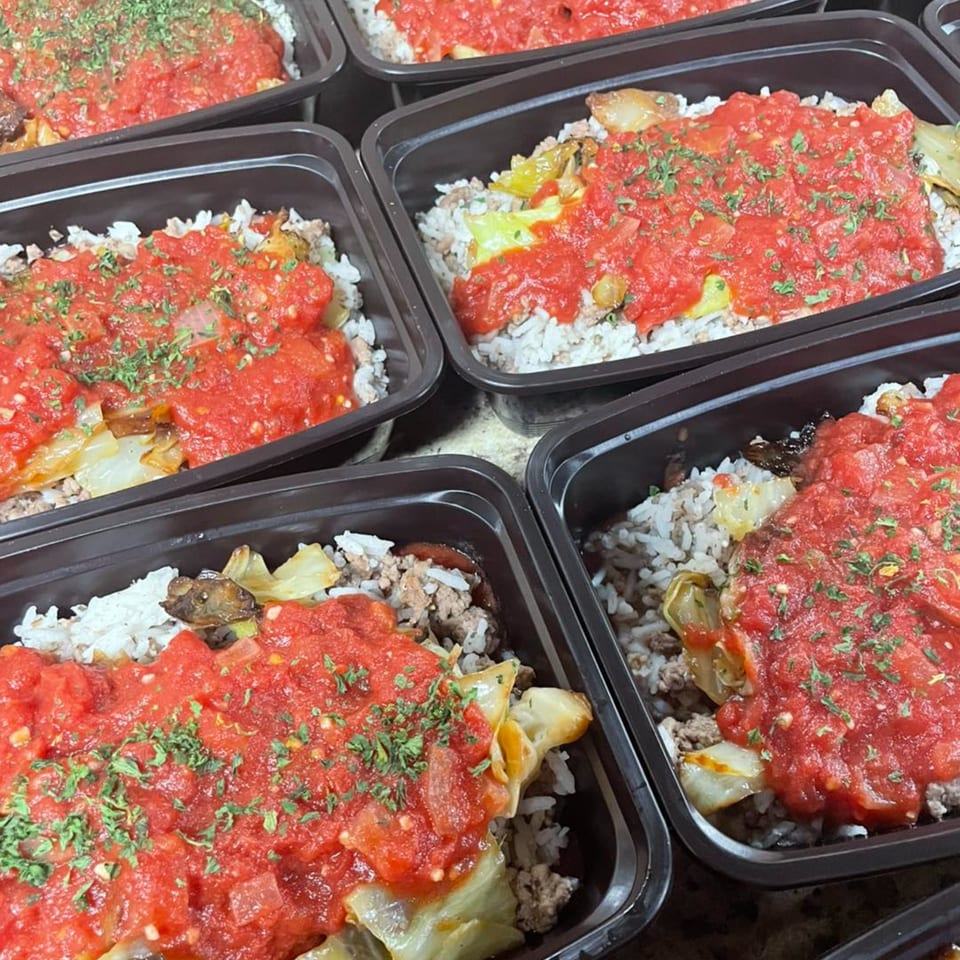 Several black containers filled with rice, ground meat, cabbage, and tomato sauce with herbs.
