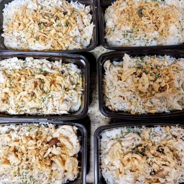 Six black containers filled with creamy chicken and rice, topped with crispy fried onions and parsley.