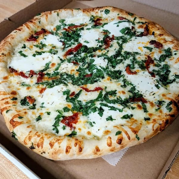 Only Pans' white pizza with ricotta, mozzarella, sun-dried tomatoes, and fresh basil in a delivery box.